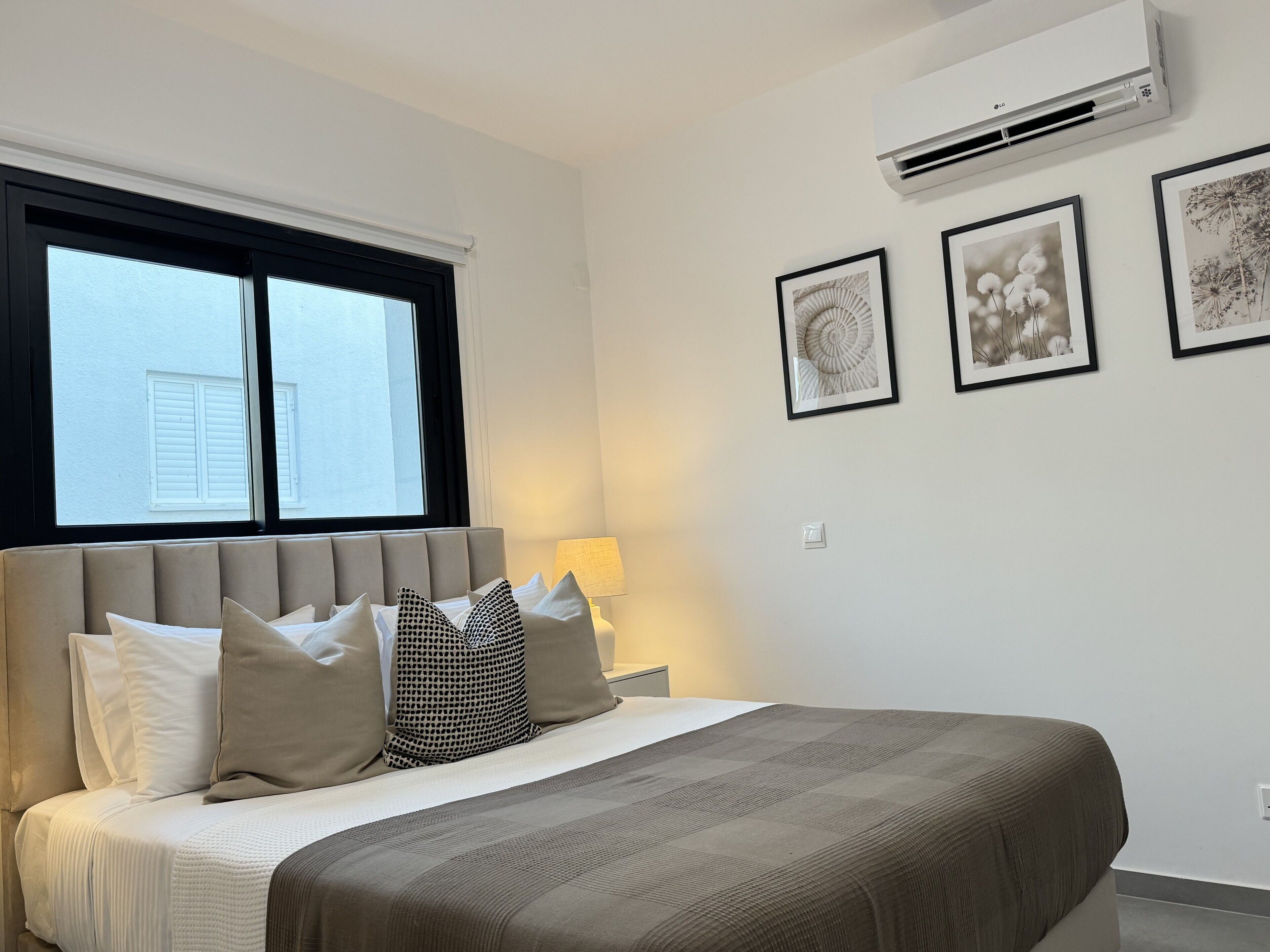 A bedroom with a bed, a window, an air conditioner, and framed pictures on the wall.