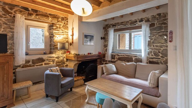 A cozy living room with stone walls, a fireplace, a sofa, a coffee table, and a television.