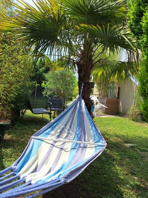 Eine Hängematte, die an einer Palme in einem Garten befestigt ist, mit Stühlen und einem kleinen Tisch.