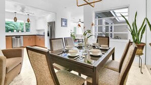 A modern kitchen with white cabinets, a dining area with a glass table, and a view of a lush garden through large windows. - Bungalow 31 – Coral Ridge Oasis | Heated Pool, Private Escape, Just 6 Mins to the Beach! (Fort Lauderdale)