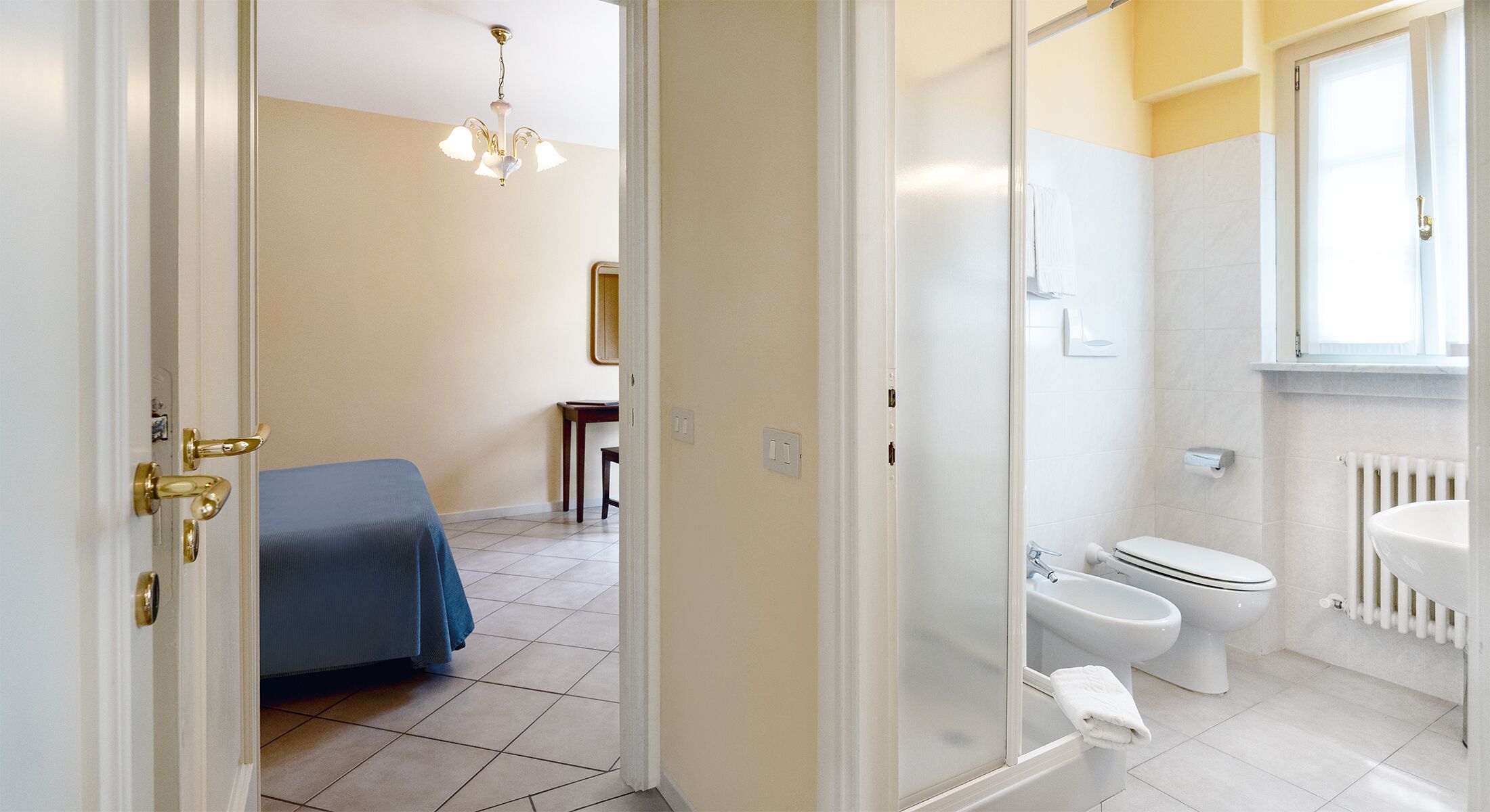 Una camera d'albergo con un letto, un bagno con il water, un lavandino e una doccia.