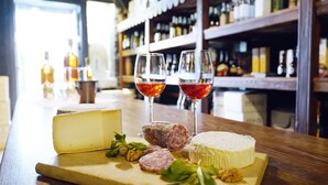A cheese board with various cheeses and meats, two glasses of red wine, and a bar in the background. - Residenza dei Fiori (Cannero Riviera)