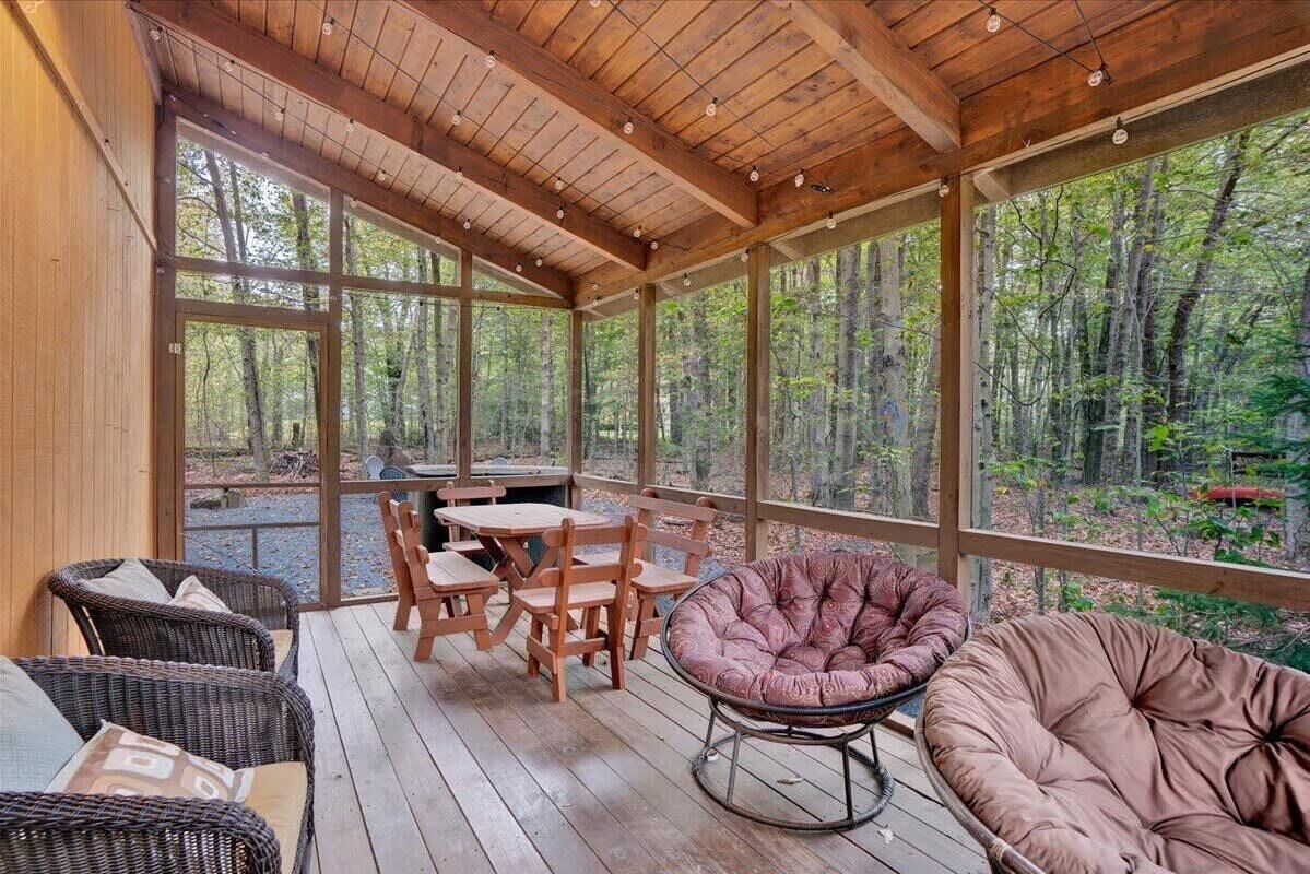A covered outdoor area with a wooden deck, a table with chairs, and a cushioned seating area.