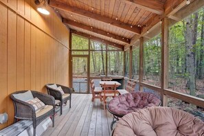 A covered outdoor seating area with wicker furniture and a cushioned bench, surrounded by wooden walls and large windows.