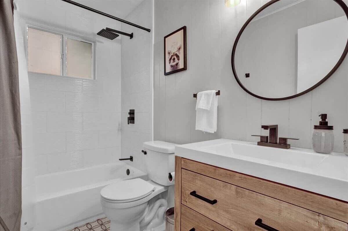 Ein Badezimmer mit Toilette, Badewanne, Waschtisch mit Spiegel und einem gerahmten Bild an der Wand.