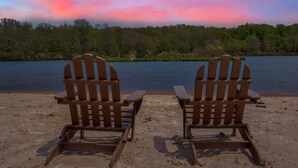 Two wooden Adirondack chairs facing a lake with a forested shoreline.