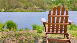 A wooden Adirondack chair facing a lake with a forested background.
