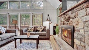 A cozy living room with a stone fireplace, large windows, and a comfortable sofa.