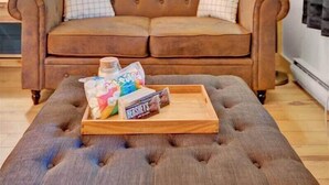Et hyggeligt rum med en brun lædersofa, en pufs med snacks og en blå væg.