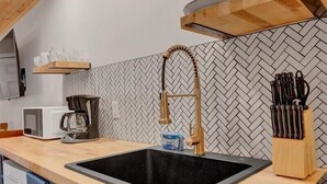 Et køkken med træloft, backsplash i fiskebensmønster, en sort vask og en holder til køkkenredskaber i træ.