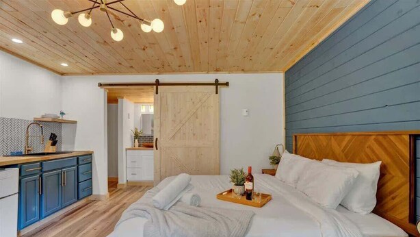 Ein Schlafzimmer mit Holz-Kopfteil, einem Bett mit weißen Bettwäsche, einem Nachttisch und einer Ablage mit Flasche und Gläsern.