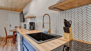 Eine moderne Küche mit Fischgrätmuster-Fliesen an der R ückwand, einem schwarzen Spülbecken, Holzschränken und einer Holzbalkendecke.