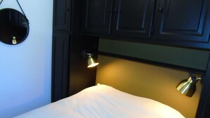 A small, dimly lit room with a single bed, a round mirror, and two wall-mounted lamps. - Châtel Apartment 2 rooms - 4 people, near ski lift (Châtel)