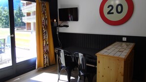A room with a dining table, chairs, a TV mounted on the wall, and a speed limit sign. - Châtel Apartment 2 rooms - 4 people, near ski lift (Châtel)
