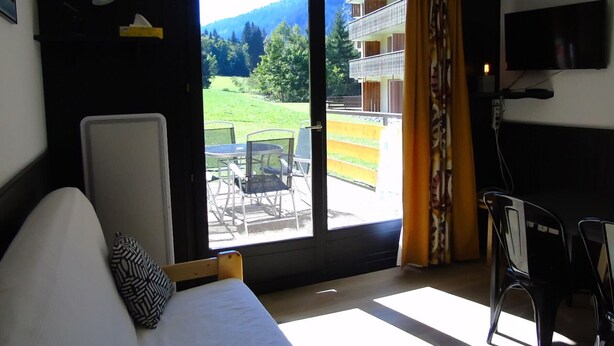 A room with a bed, a desk, and a chair. There is a sliding glass door leading to a balcony with outdoor furniture. - Châtel Apartment 2 rooms - 4 people, near ski lift (Châtel)
