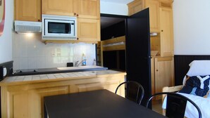 A compact kitchen with wooden cabinets, a microwave, a sink, and a black refrigerator. There is a small dining table with chairs. - Châtel Apartment 2 rooms - 4 people, near ski lift (Châtel)