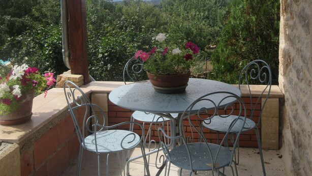 An outdoor patio with a round metal table and four chairs, surrounded by potted plants and a view of greenery. - Gîte Dans Maison en Pierre, Avec Piscine, à la Campagne, Proche Villefranche (Savignac)