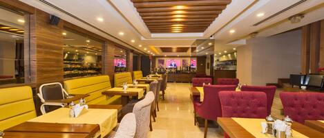 A restaurant with booths and tables, wooden ceiling, and a bar area in the background.