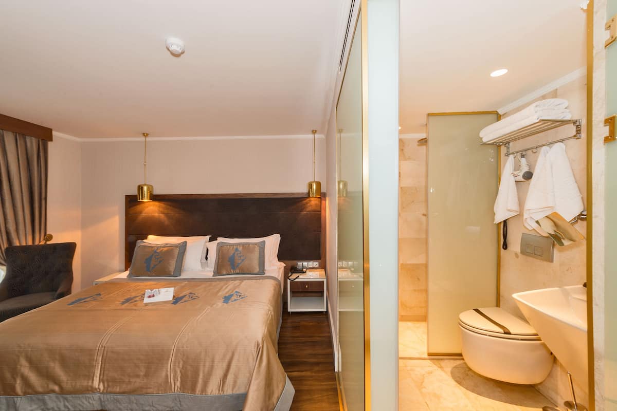 A hotel room with a bed, bedside table, nightstand, and a bathroom with a toilet, sink, and towel rack.
