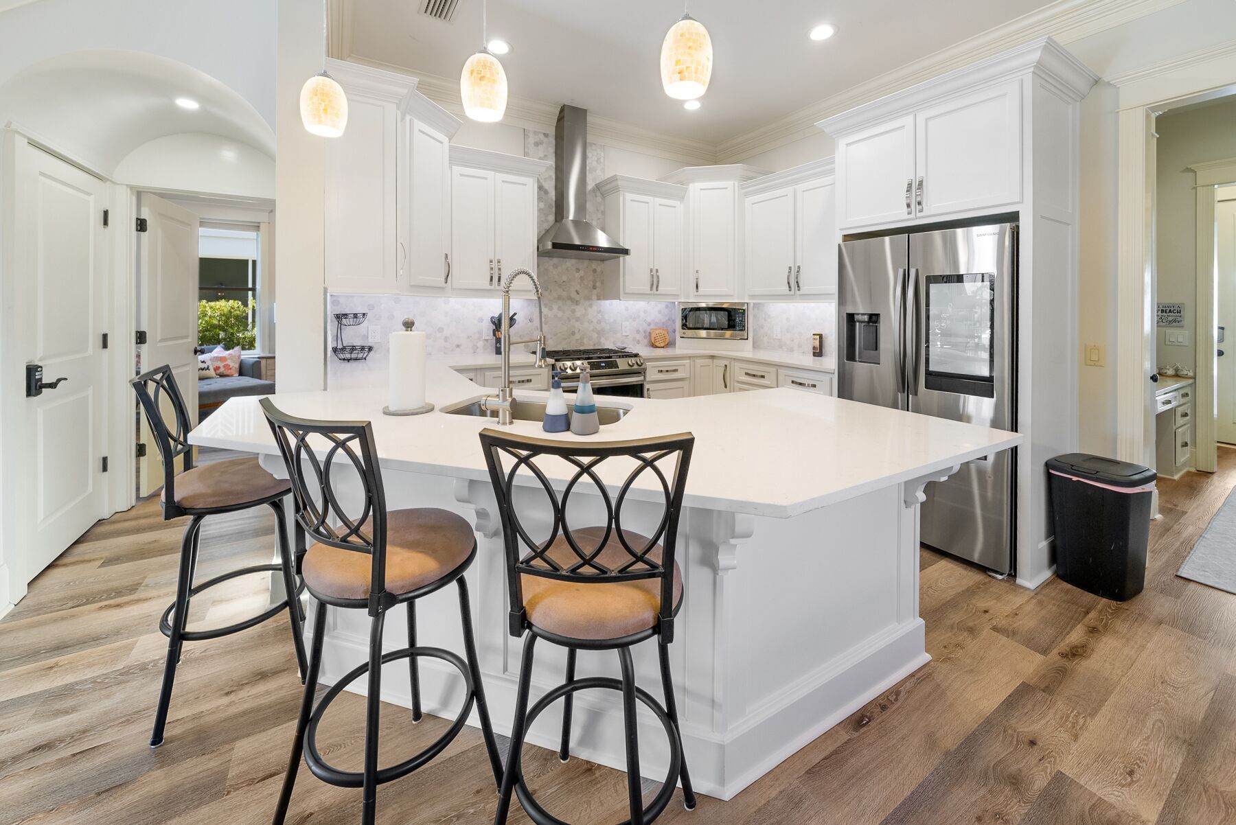 A spacious kitchen with white cabinetry, a large island with bar stools, stainless steel appliances, and pendant lighting.