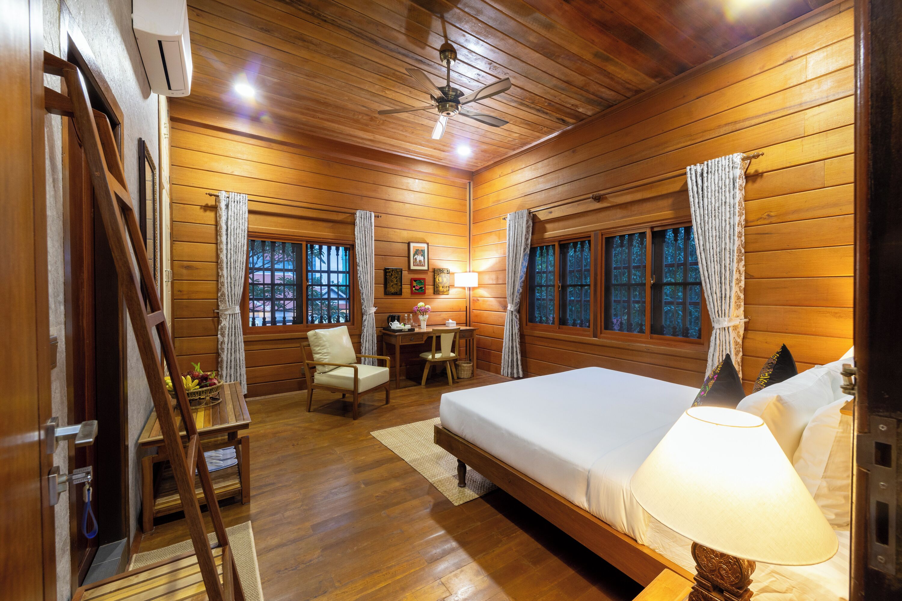 A wooden cabin room with a bed, desk, chair, and a ladder.