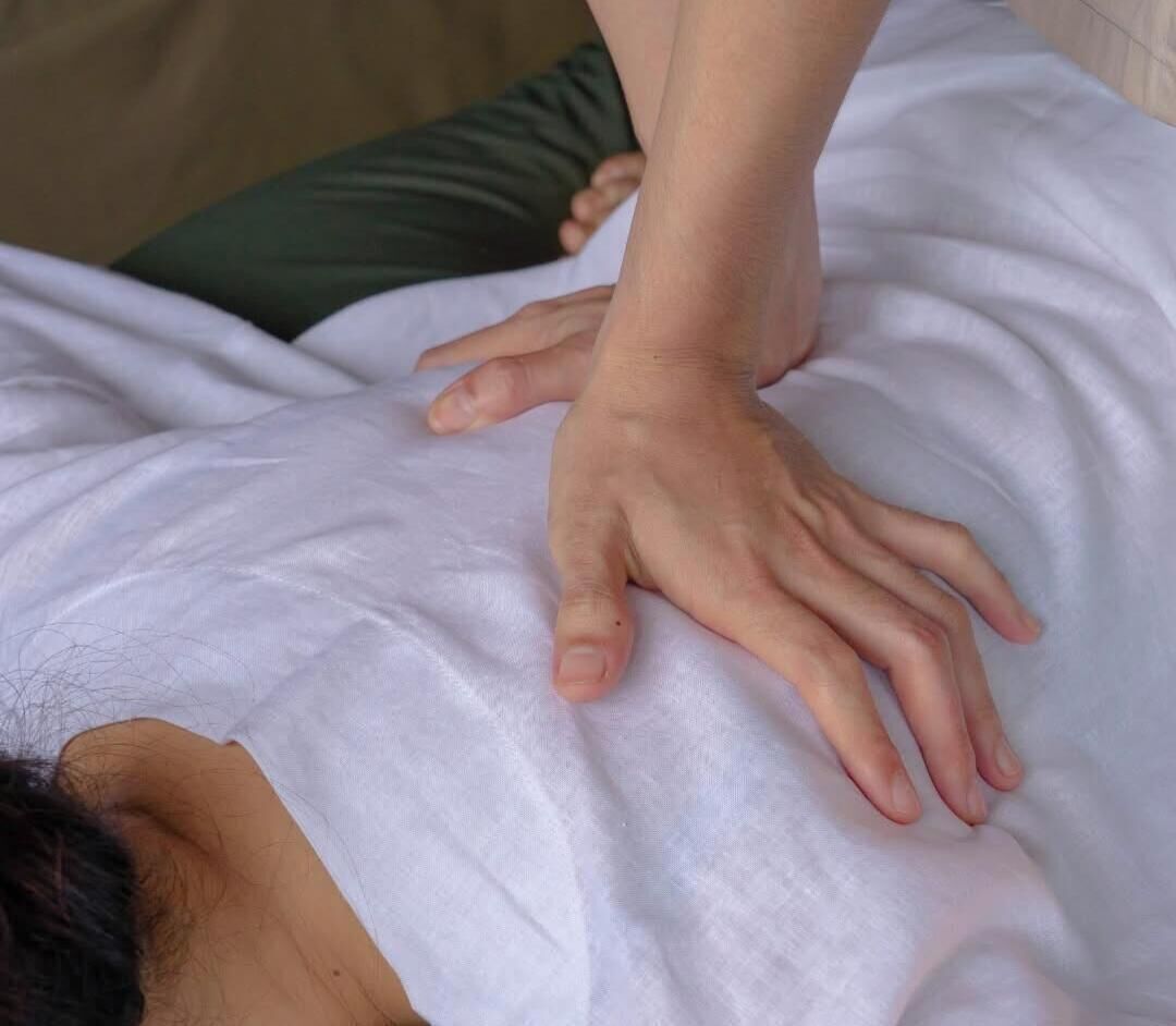 A person receiving a massage on a bed with a white sheet.