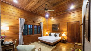 A wooden cabin bedroom with a bed, bedside tables, a desk, and a chair. - Atoh's Maison (Siem Reap)