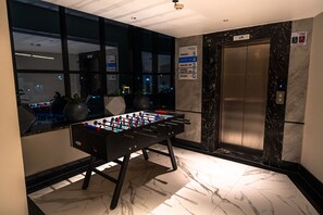 Un vestíbulo con una mesa de fútbol de mesa, un ascensor y un cartel con los números de las habitaciones.