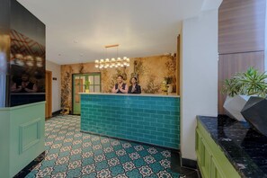 A reception area with a teal reception desk, patterned floor tiles, a green door, and a hanging light fixture.