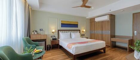 Una habitación de hotel con cama, escritorio, silla, armario y ventilador de techo.