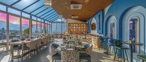 Un restaurante con techo alto, amplios ventanales y vistas a las montañas.