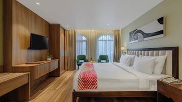 Habitación de hotel con piso de madera, cama con manta estampada, televisor en la pared y una silla verde.