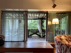 Una habitación con piso de madera, un sofá, una lámpara y vista a un jardín por una puerta corrediza.