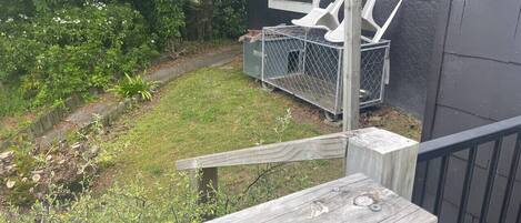 A wooden deck with a metal railing, a small garden with grass and shrubs, and a window with a chair outside.