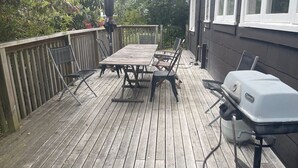 Una terraza de madera con una mesa, sillas, una parrilla y un parasol colgante.