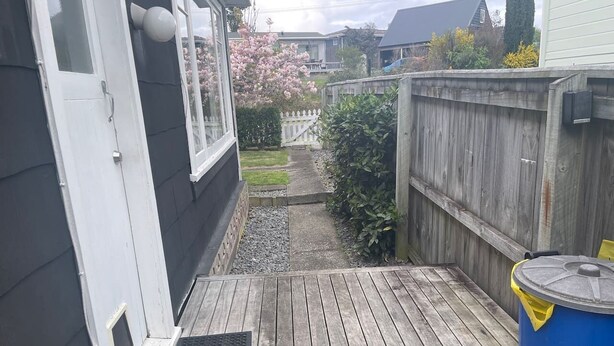 Una terraza de madera con una rejilla metálica, un barril azul y una valla blanca al fondo.