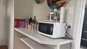 Una cocina con un microondas blanco sobre una encimera blanca, una tabla de cortar rosa y varios utensilios de cocina.