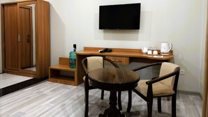 Habitación de hotel con un escritorio de madera, dos sillas, un televisor, un armario y una botella de agua.