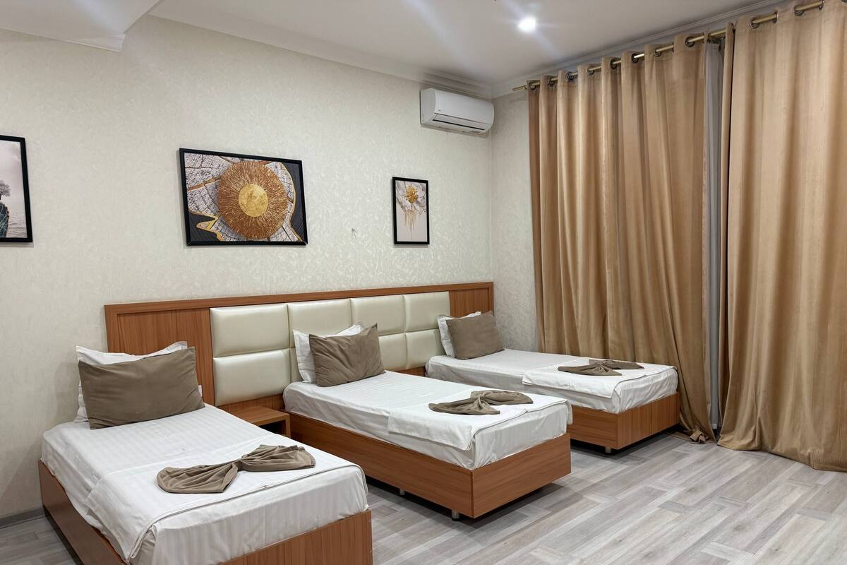 A hotel room with two single beds, a wooden headboard, beige curtains, and two framed artworks on the wall.