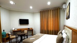 Una habitación de hotel con cama, escritorio, silla, televisor y dispensador de agua.