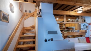 Een rustiek interieur met een houten trap, een schouw van baksteen en een keuken met houten kasten en een witte bank.