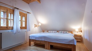 Een slaapkamer met een schuine plafond, houten bedframe, witte beddengoed, een radiator en twee bedlampen.