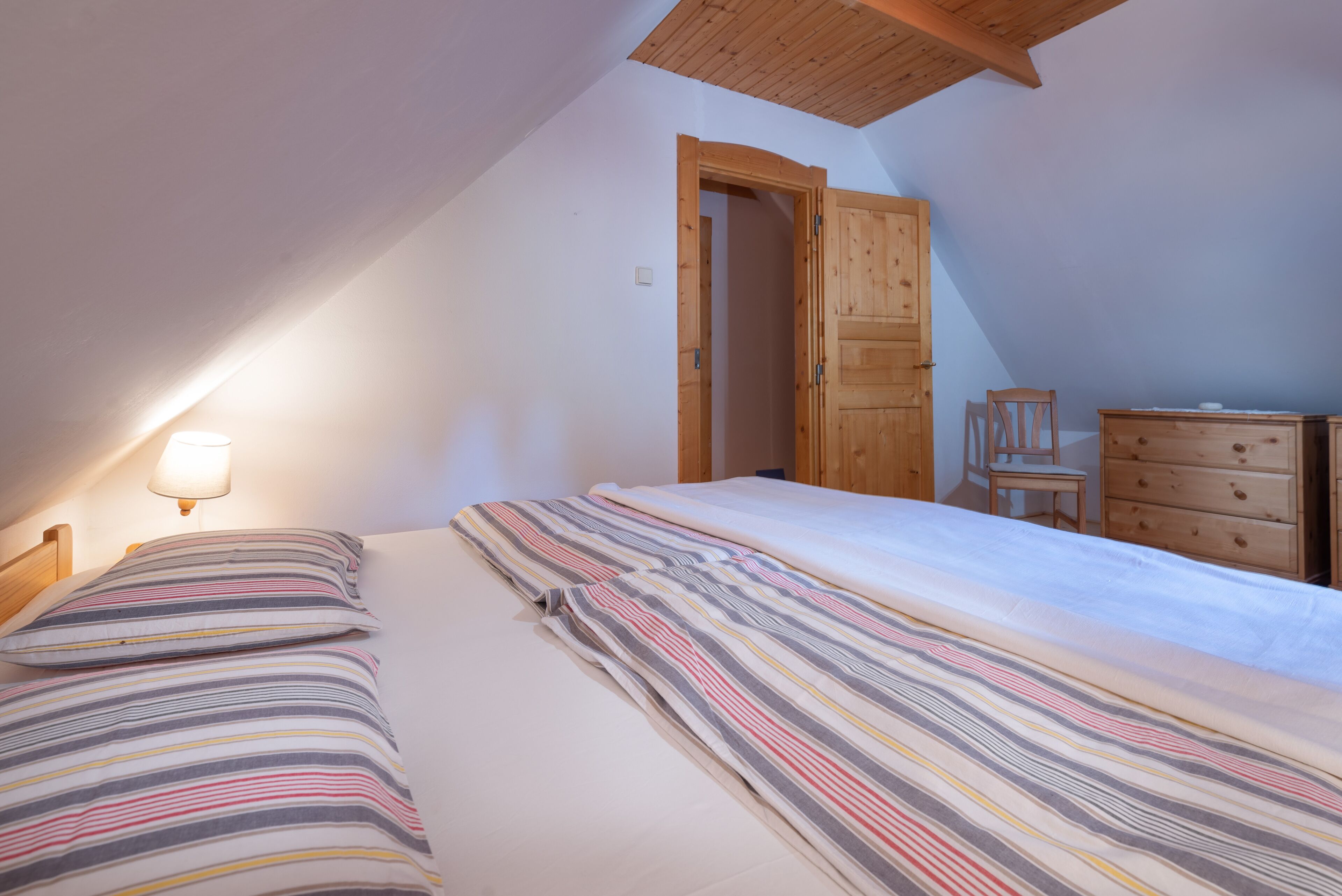 A bedroom with a bed, a wooden dresser, a chair, and a lamp.