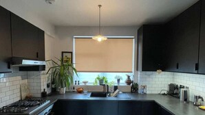 A modern kitchen with dark cabinetry, a central island, a gas stove, and a window providing natural light. - Contemporary 1BD Flat W/balcony - Stoke Newington! (London)