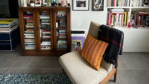 A living room with a sofa, a bookshelf, a TV, and framed pictures on the wall. - Contemporary 1BD Flat W/balcony - Stoke Newington! (London)