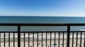 A beach view from a balcony with a railing, ocean, and beachgoers. - Oceanfront Efficiency  Stunning View12th Floor (Myrtle Beach)
