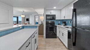 Een moderne keuken met witte kasten, een zwarte koelkast en een blauwe tegelachtergrond.