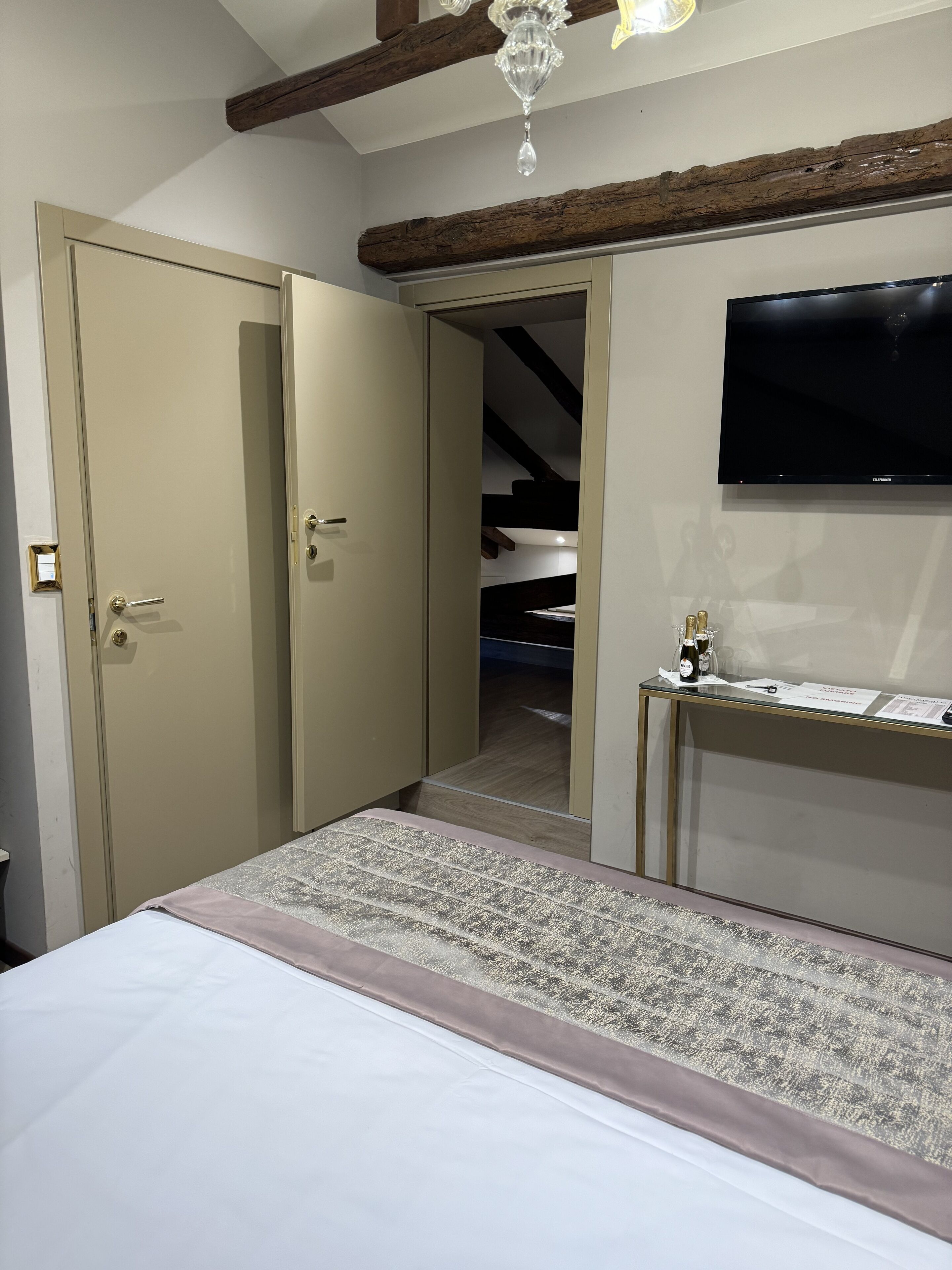 A bedroom with a bed, a wardrobe, a desk with a flat-screen TV, and a staircase leading to an upper level.