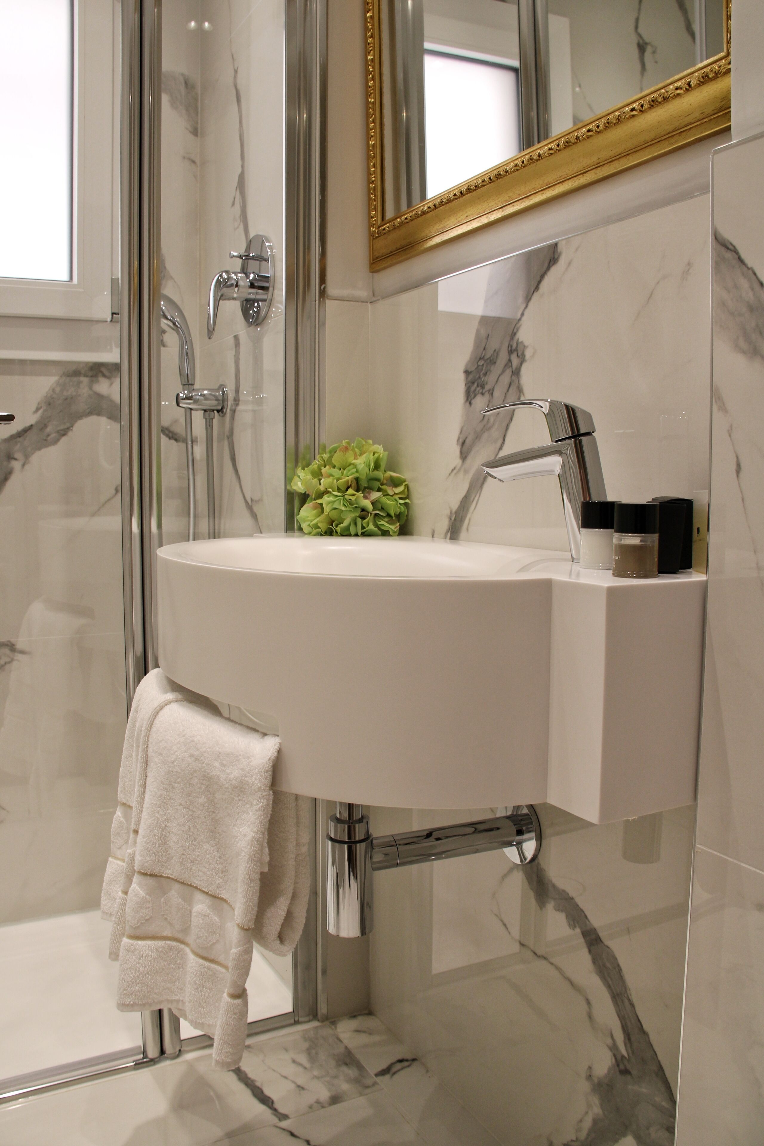 A bathroom with a glass-enclosed shower, a white sink, and a gold-framed mirror.