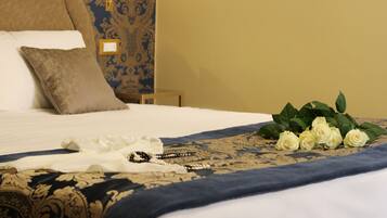 A neatly made bed with a blue and gold patterned bedspread, a white pillow, and a bouquet of white roses.